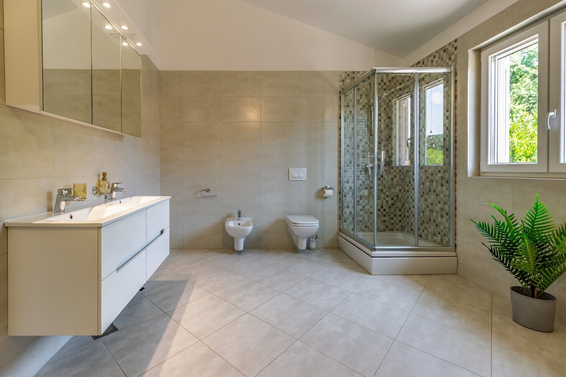 Een moderne badkamer met een grote spiegel, een witte wastafel, een toiletbril en een douche met glazen wanden.