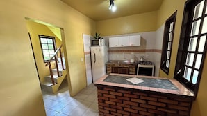 A kitchen with a central island, a refrigerator, a stove, and cabinets. There is a window with blinds and a door leading to another room. - Residencial Villa Luana (Garopaba)