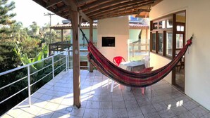 A balcony with a hammock, a table, and chairs. - Residencial Villa Luana (Garopaba)