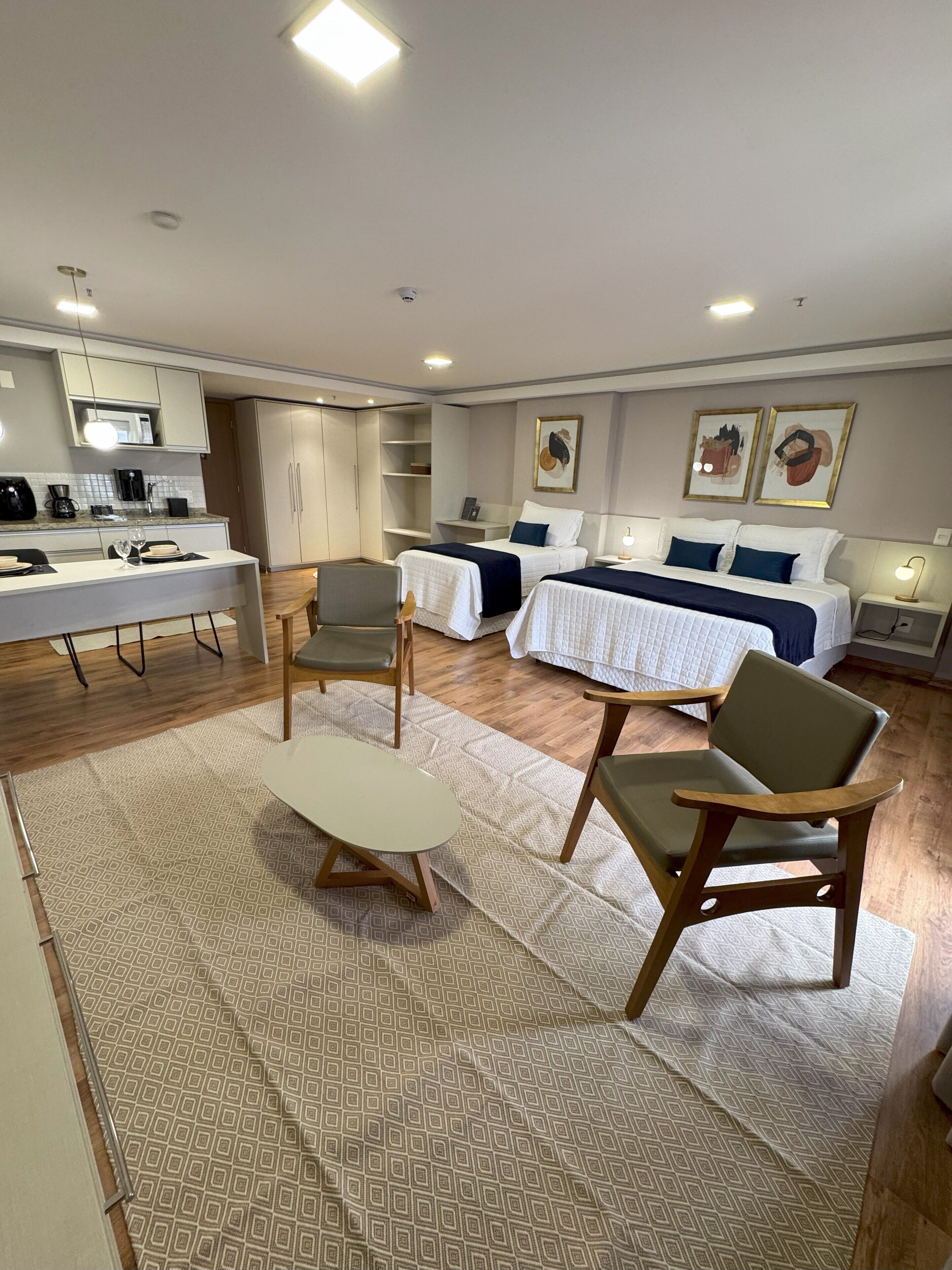 Habitació d'hotel moderna amb cuineta, dos llits, zona de dinar i saló amb taula i cadires.