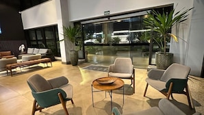 A modern indoor seating area with sofas and a coffee table, large windows, and potted plants. - Hotel Flat Afonso Pena by FGibran (Campo Grande)