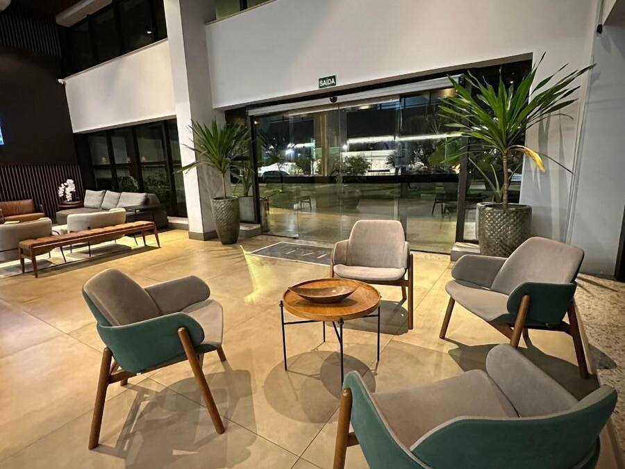 Un área de estar interior moderna con sofás, una mesa de centro, ventanas amplias y plantas en macetas.