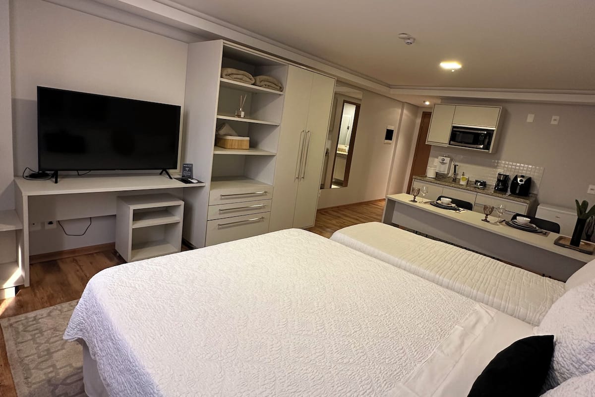 Un dormitorio moderno con una cama grande, televisión, armario y zona de cocina.