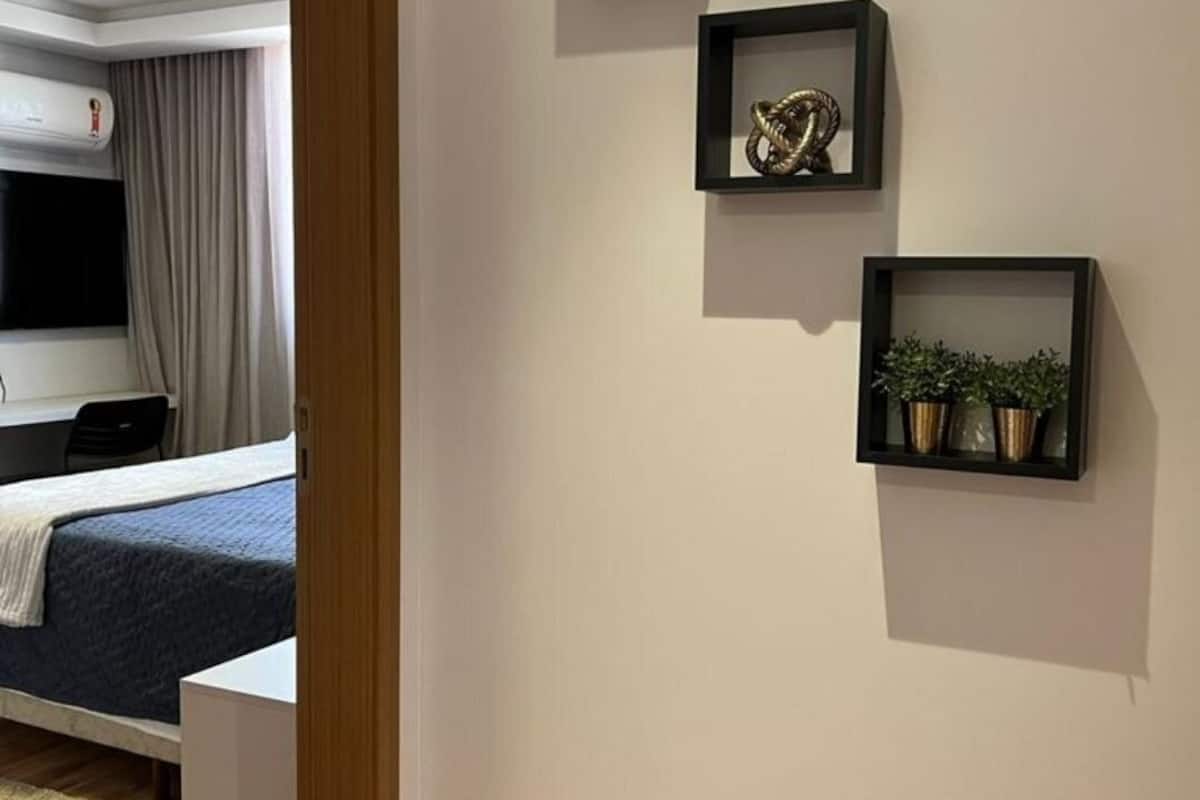 Habitación de hotel con cama, televisor, equipo de aire acondicionado y tres estantes con adornos.