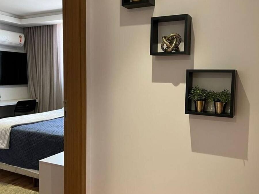 Hotelkamer met een bed, een televisie, een airconditioning en drie wandplanken met decoratieve objecten.