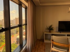 Una habitación con ventanas amplias, un televisor sobre un mueble, una silla y una planta.