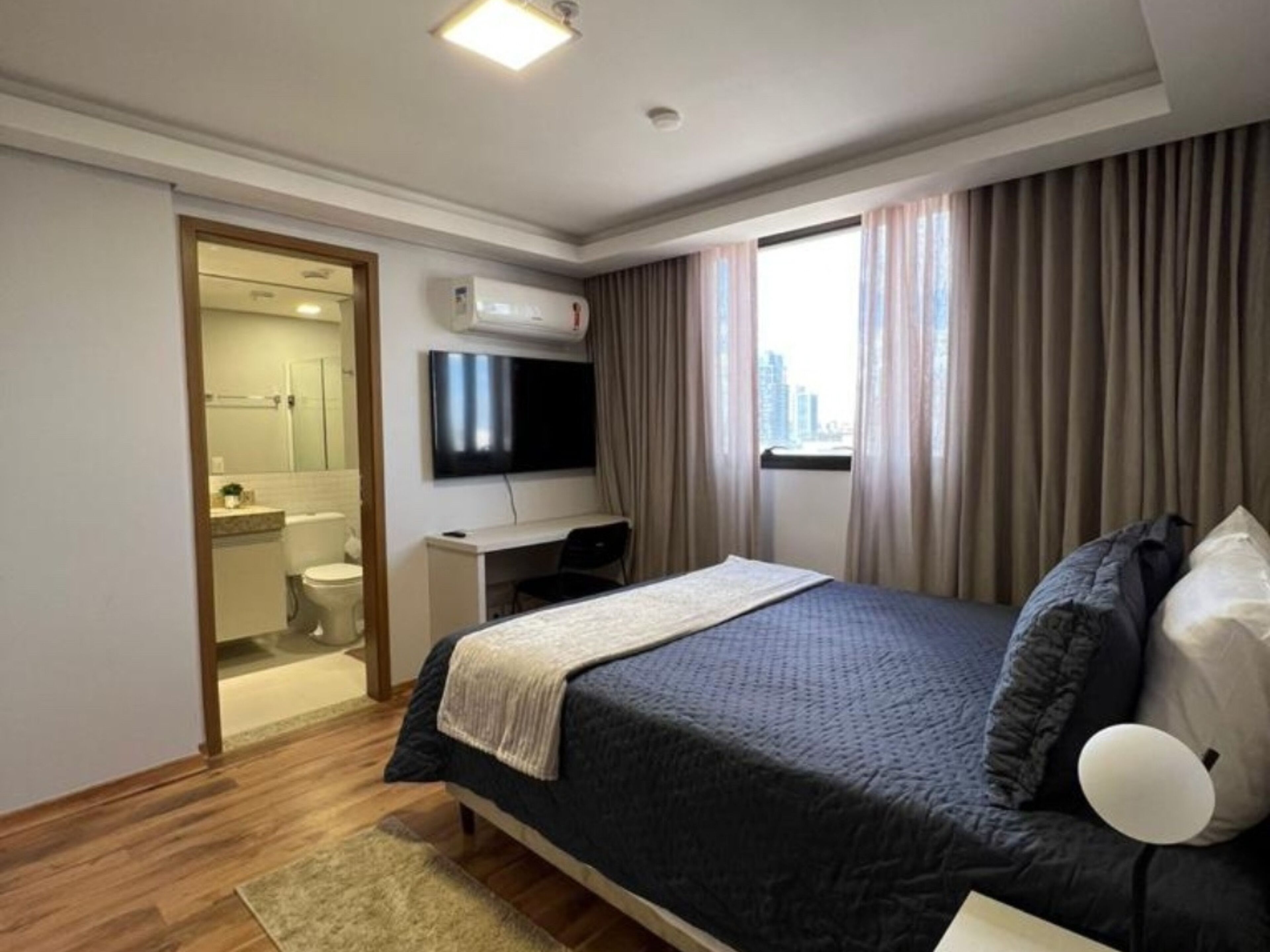 A hotel room with a bed, a desk, a TV, and a bathroom visible through an open door.