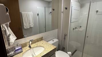 A modern bathroom with a granite countertop sink, a toilet, a glass shower enclosure, and a mirror.
