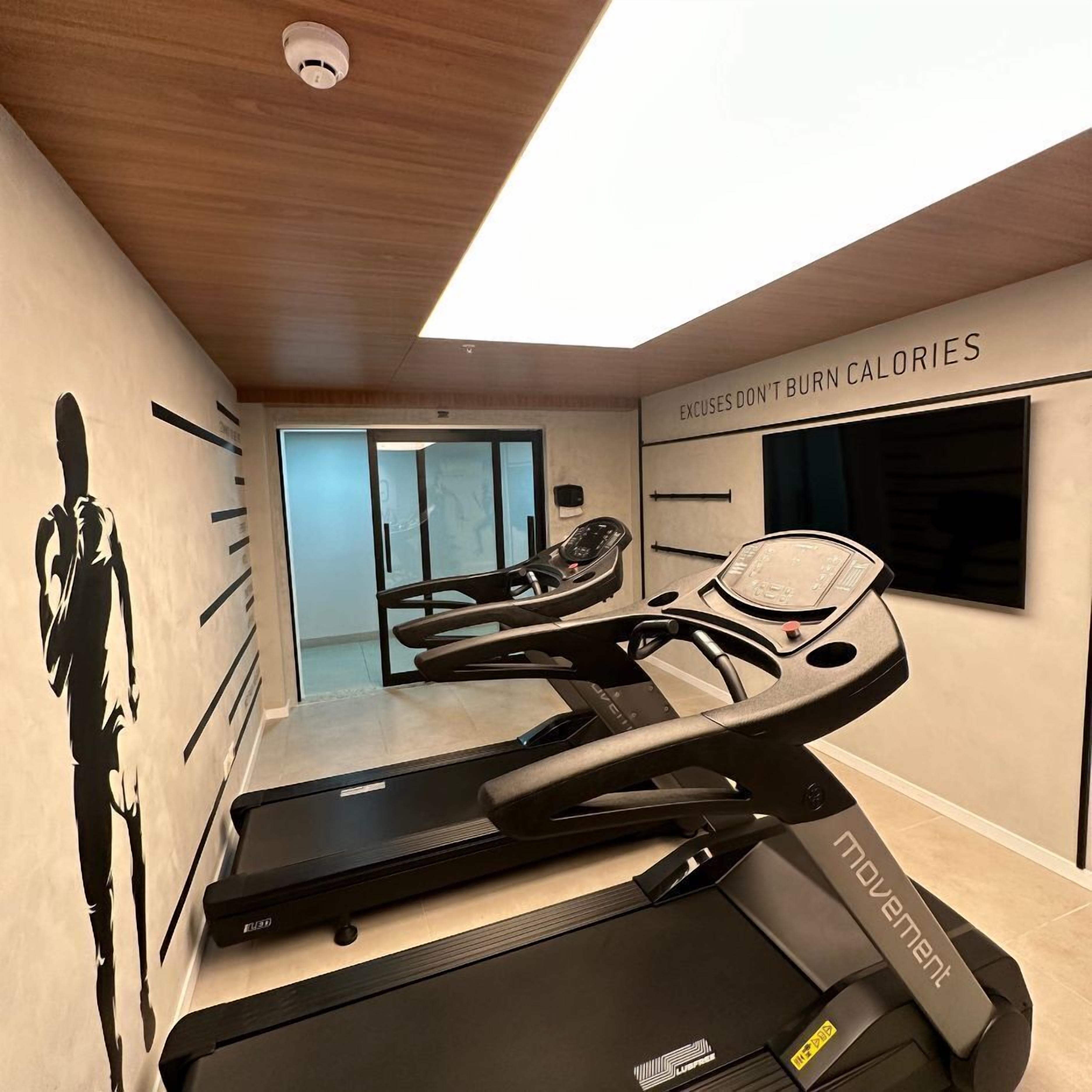 A home gym with a treadmill, stationary bike, and a wall with motivational text.