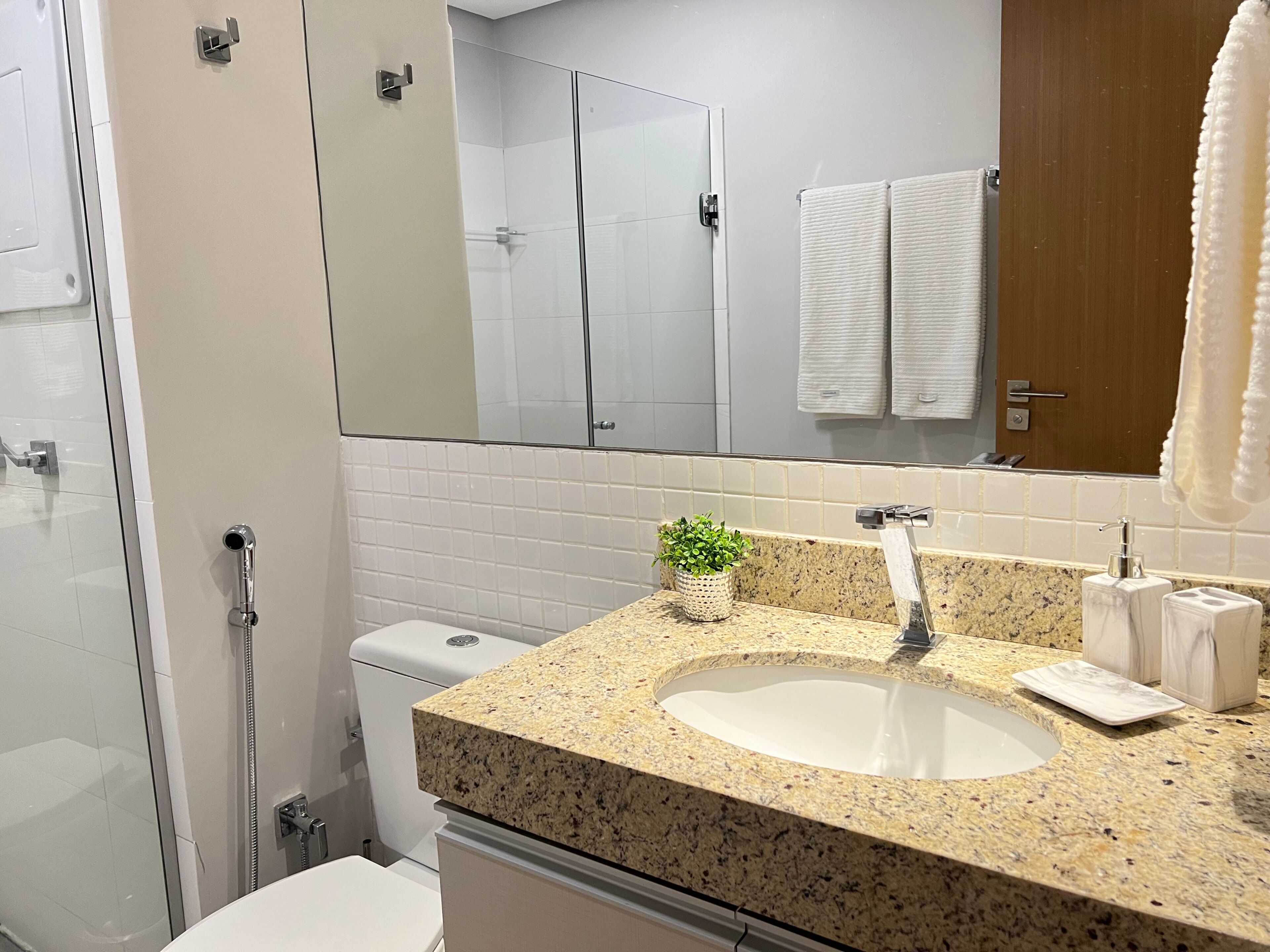 A modern bathroom with a granite countertop sink, a glass shower enclosure, and a white toilet.
