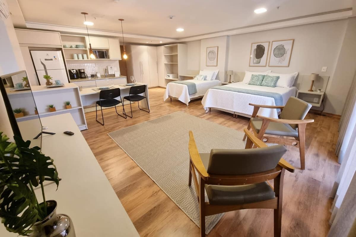 Una habitación moderna y luminosa con cocina, dos camas, zona de comedor y un ventanal grande.