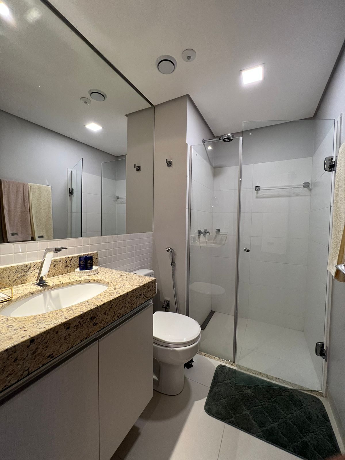 Un baño moderno con encimera de granito, inodoro, cabina de ducha de vidrio y espejo.
