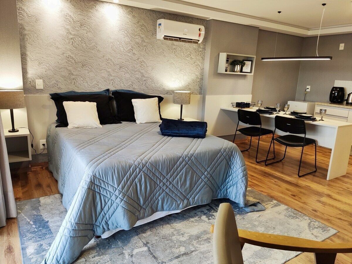 A modern bedroom with a bed, bedside tables, a desk, chairs, and an air conditioning unit.