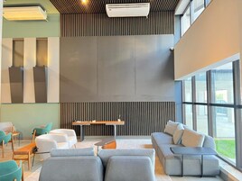 Un área de descanso moderna con asientos, una mesa central y ventanas amplias que permiten la entrada de luz natural.