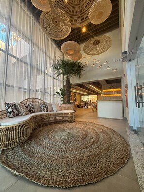 Un hall espacioso con un tapete tejido grande, una zona de estar con cojines y una palmera alta.