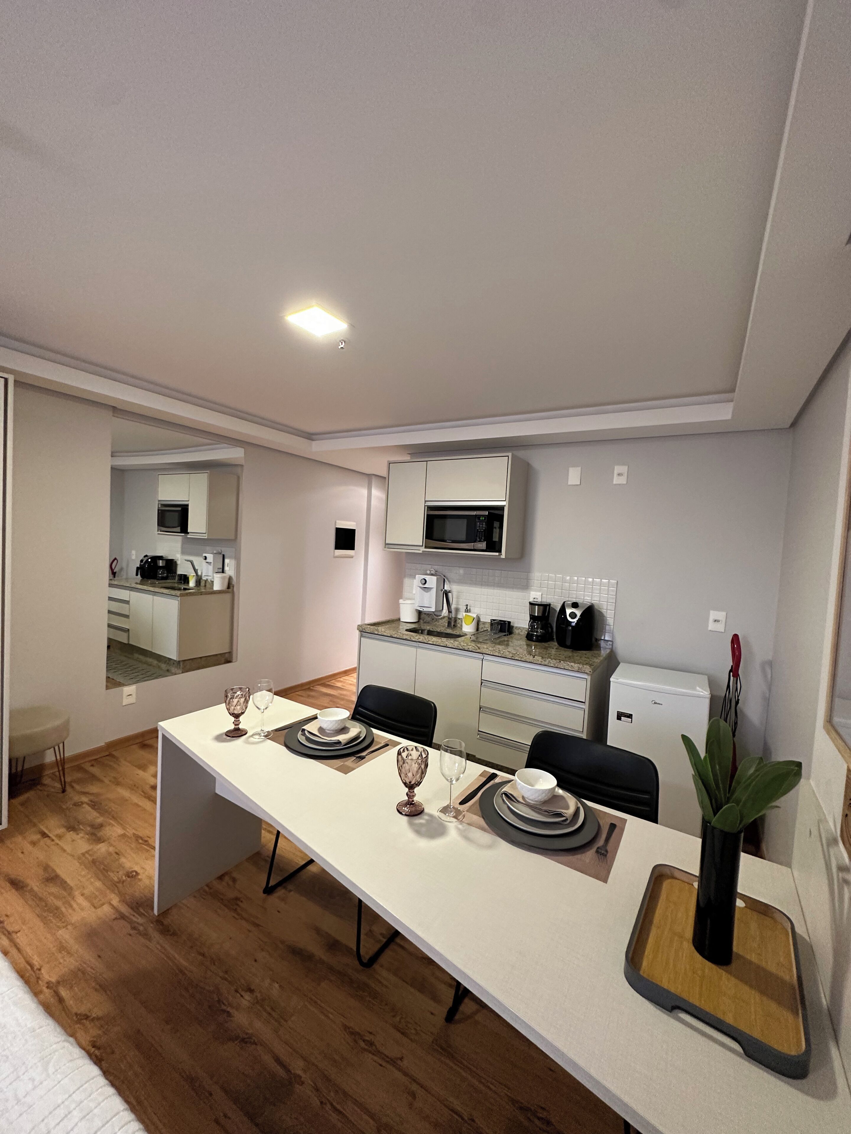 Cocina compacta con armarios blancos, microondas y refrigerador. Una mesa de comedor con sillas está colocada en el centro.