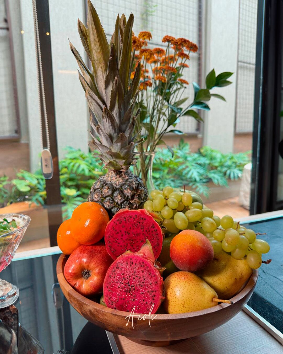 Un tazón de madera lleno de frutas y una piña sobre una mesa.