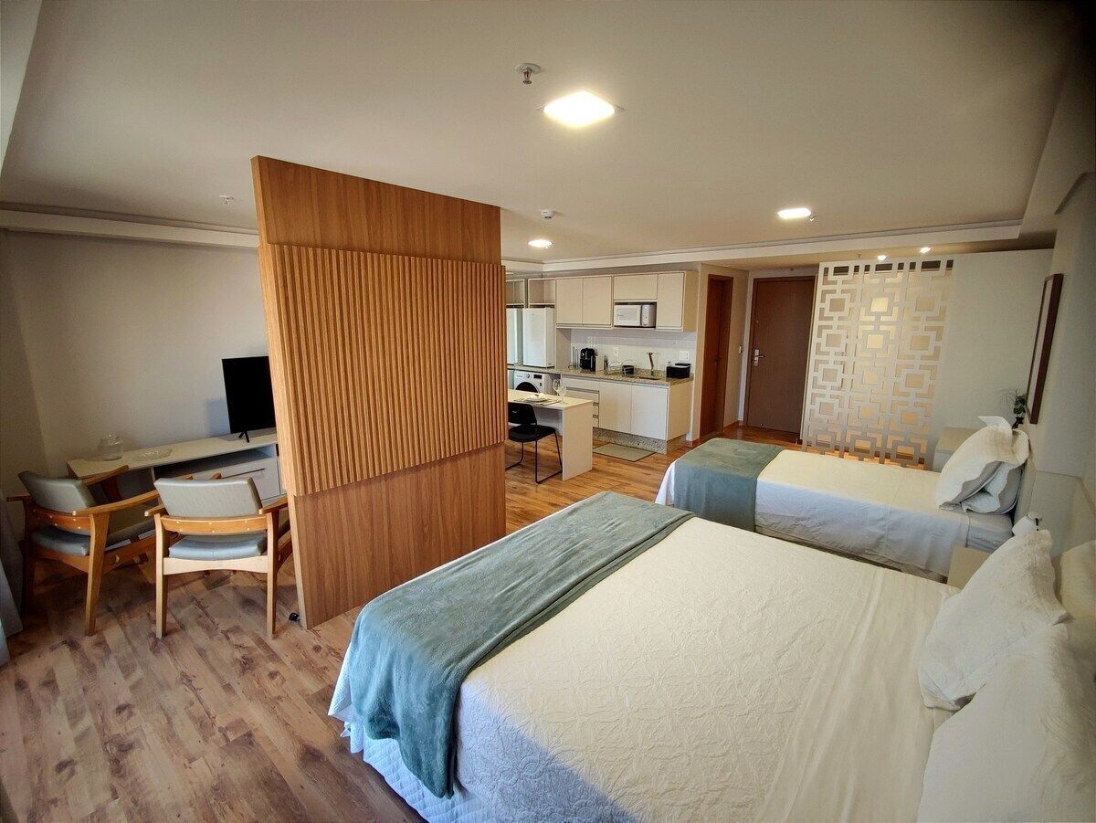 Quarto de hotel com duas camas, uma escrivaninha e uma cozinha compacta.