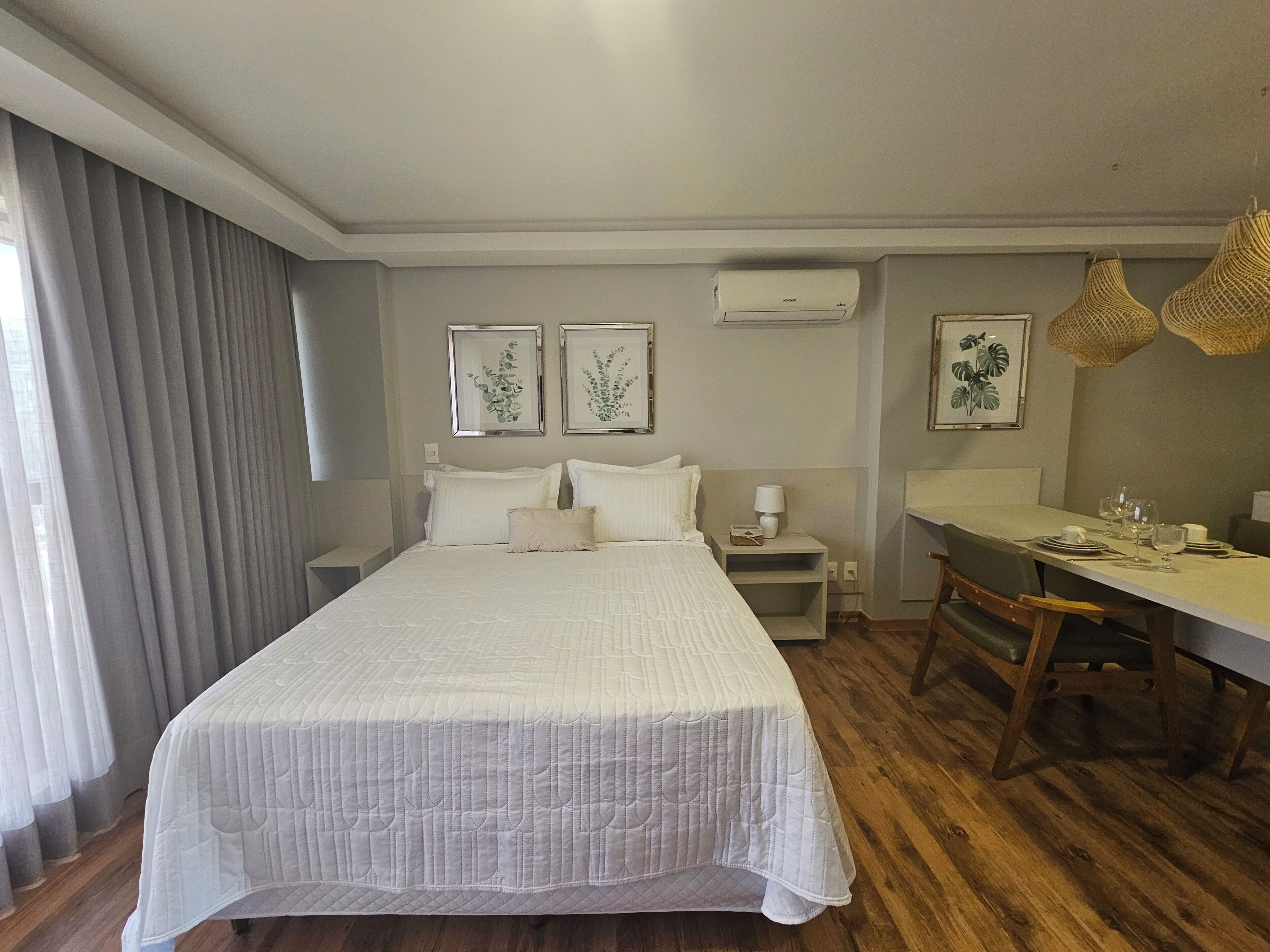A hotel room with a large bed, a desk, and two framed botanical prints on the wall.
