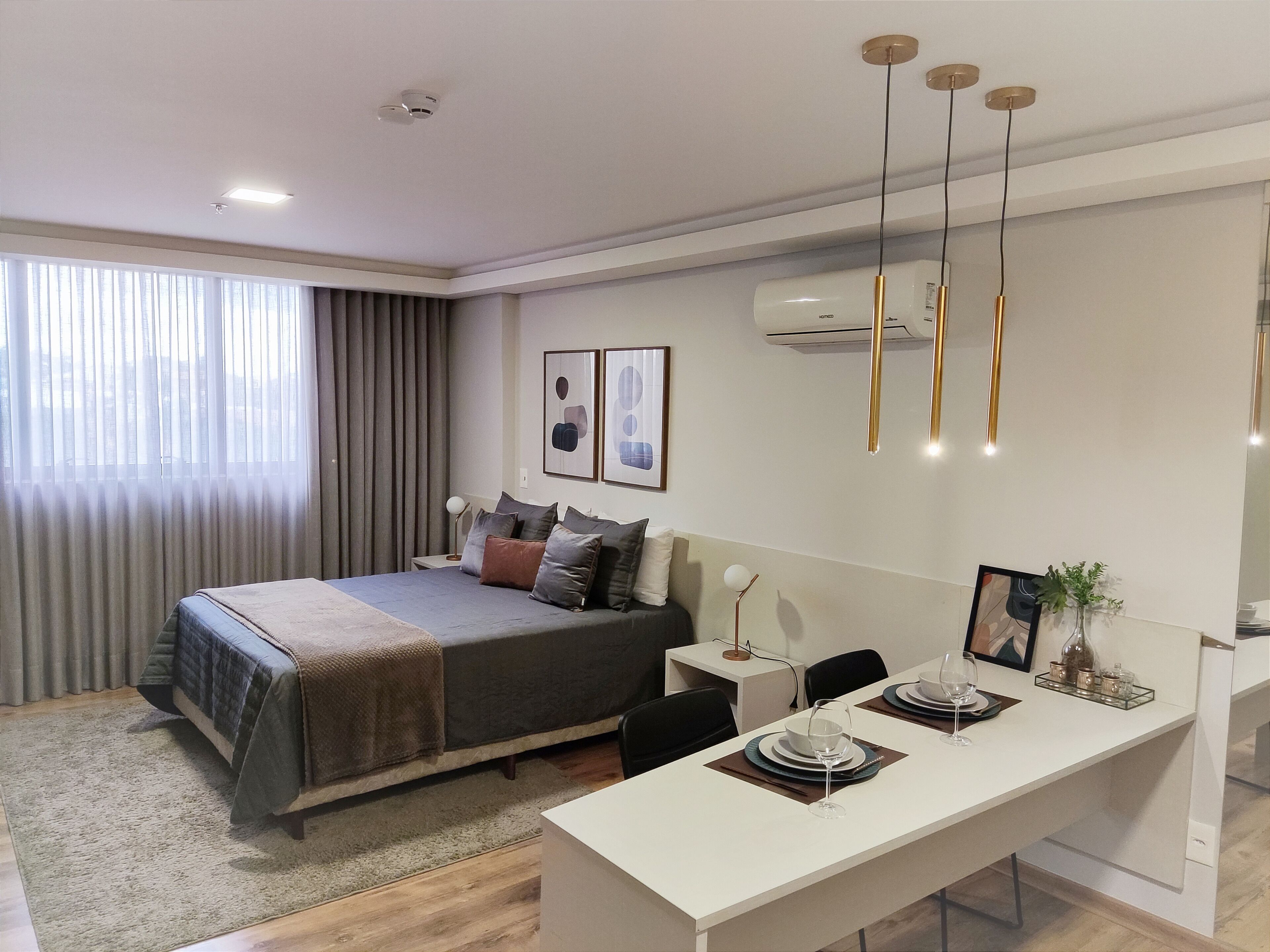 A modern hotel room with a neatly made bed, a dining table set for two, and a large window with curtains.