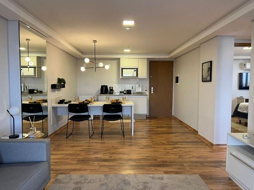 A modern living room with a dining area, wooden flooring, and a kitchen in the background.