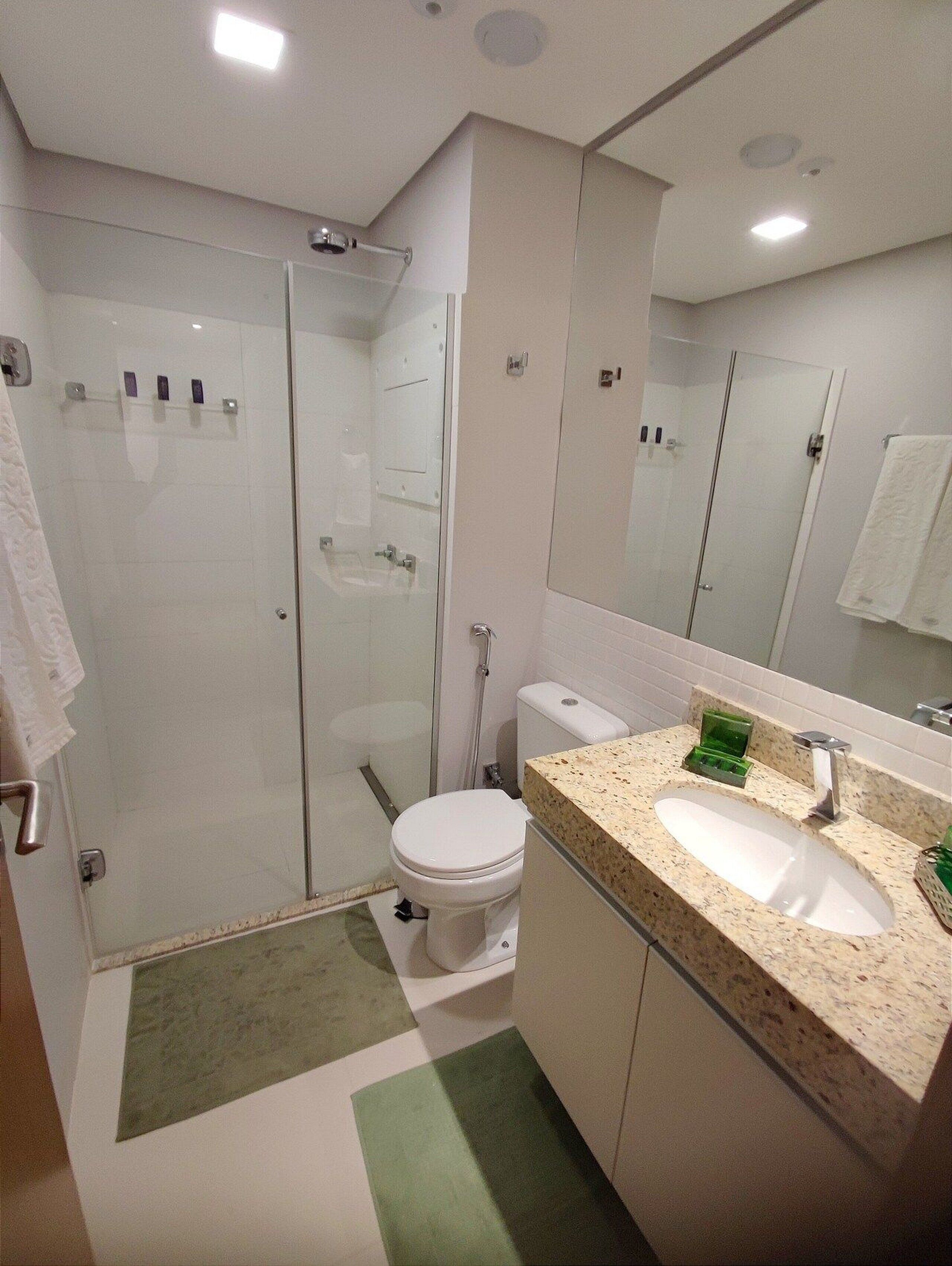 Casa de banho moderna com chuveiro envolto em vidro, sanita branca e lavatório com bancada de granito.