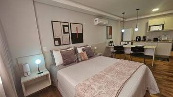 A modern bedroom with a large bed, bedside tables, a desk, and a kitchenette.