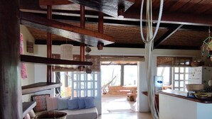 Un amplio salón con techo alto, vigas de madera, un sofá con cojines, una silla colgante y vistas al exterior.