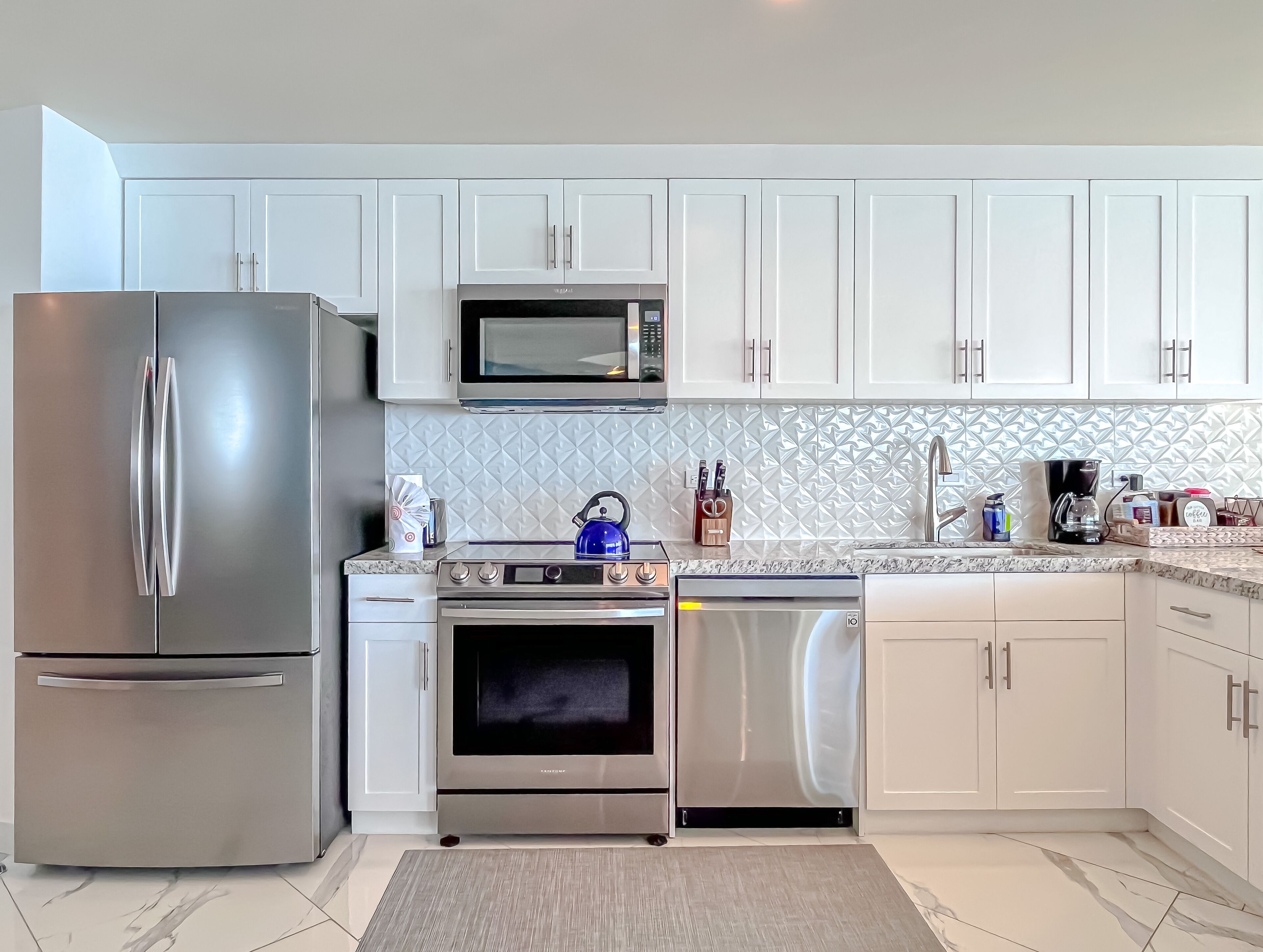 A modern kitchen with stainless steel appliances, white cabinetry, and a patterned backsplash.
