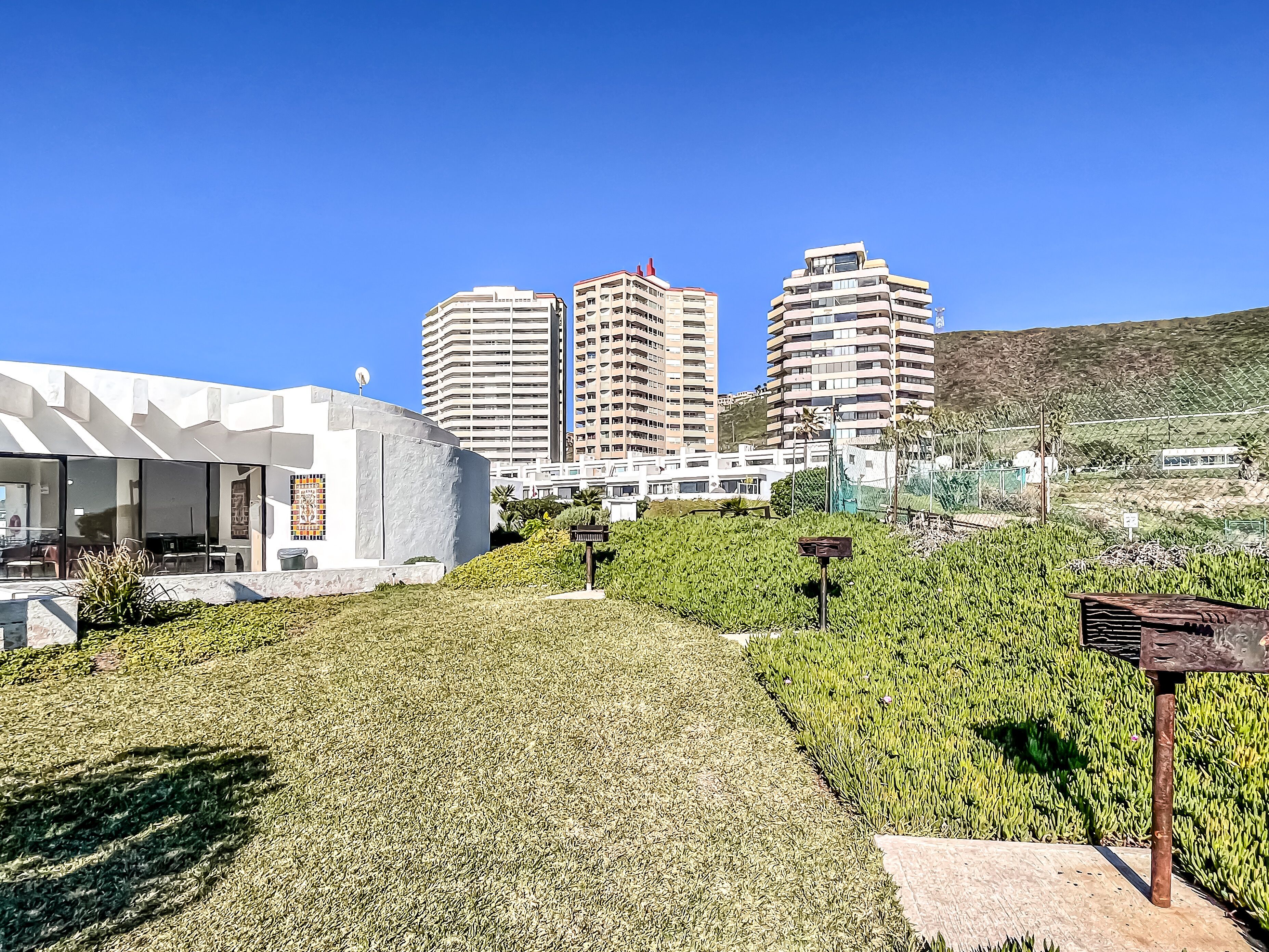 A modern building with a unique architectural design, surrounded by well-maintained greenery and tall residential buildings in the background.