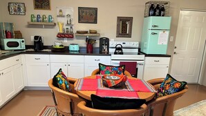 A kitchen with white cabinets, a teal refrigerator, a dining table with chairs, and various kitchen appliances. - Little Bird Casita: Have the Experience the New Mexico Traveler Hopes to Find. (Albuquerque)
