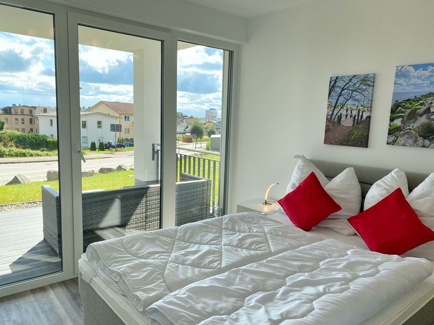 A bedroom with a large bed, a sliding glass door leading to an outdoor balcony, and two wall-mounted pictures.