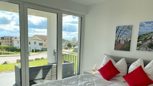 Un dormitorio con una cama grande, un ventanal corredero que da a un balcón exterior, y dos cuadros colgados en la pared.