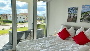 A bedroom with a large bed, a sliding glass door leading to an outdoor balcony, and two wall-mounted pictures.