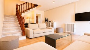 A living room with a staircase, a sofa, a coffee table, a TV, and a radiator. - Villa Toro Playa Llanes 100 m from the beach (Llanes)