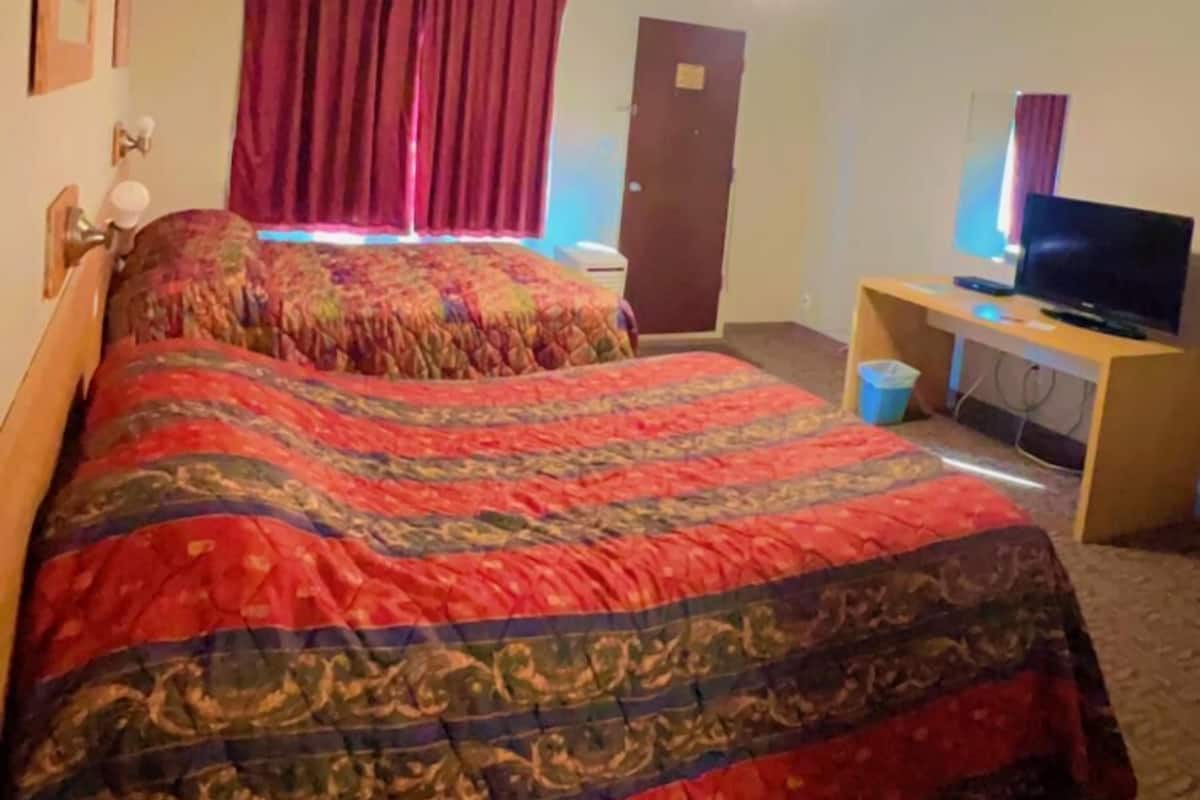 A hotel room with a bed, a desk with a computer, a ceiling fan, and a door.