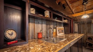 Una cocina con encimera de mármol, pileta de acero inoxidable, estantes de madera y un reloj.