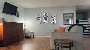 Ein Wohnzimmer mit grauem Sofa, einem kleinen runden Tisch, einer Holzkommode und abstrakter Wandkunst.