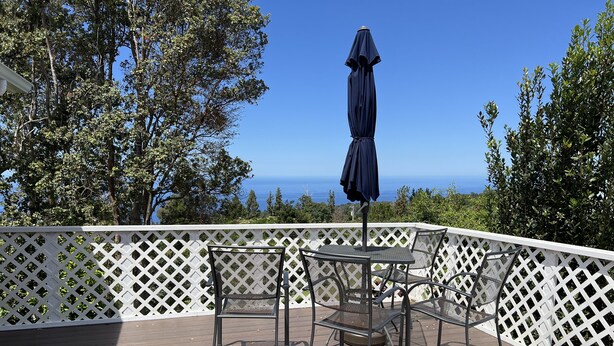 Eine Terrasse mit Tisch, Stühlen und Sonnenschirm, mit Blick auf den Ozean.