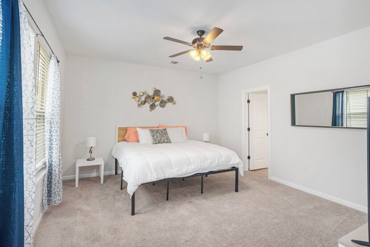 Une chambre à coucher comprenant un lit, une table de chevet, un ventilateur de plafond et un miroir fixé au mur.