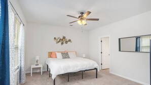 A bedroom with a bed, a nightstand, a ceiling fan, and a wall-mounted mirror. - Stylish Family Townhouse in Baton Rouge LA- BC1004 (Baton Rouge)