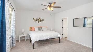 Une chambre à coucher comprenant un lit, une table de chevet, un ventilateur de plafond et un miroir fixé au mur.