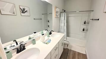 Une salle de bain avec un double lavabo, un miroir, une douche et des toilettes.