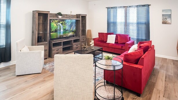 A living room with a television, red sofa, white chair, and a ceiling fan. - Stylish Family Townhouse in Baton Rouge LA- BC1004 (Baton Rouge)