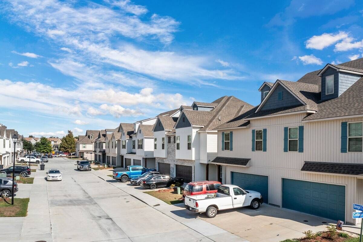 A row of townhouses with attached garages, a clear sky, and a street with parked cars.