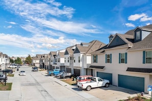 A row of townhouses with attached garages, a clear sky, and a street with parked cars.
