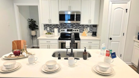 A modern kitchen with white cabinets, a stainless steel microwave, and a black stove.
