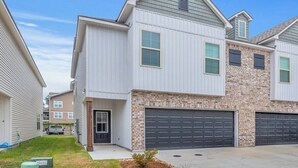 A two-story residential building with a garage, a small front yard, and a neighboring house. - Stylish Family Townhouse in Baton Rouge LA- BC1004 (Baton Rouge)