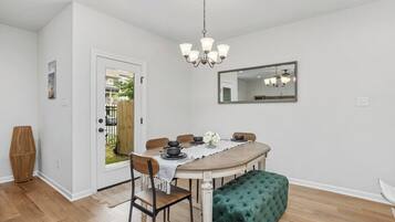 Un coin repas comprenant une table ronde, des chaises, un banc, un lustre et un miroir au mur.