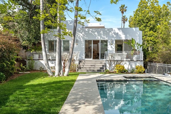 Enjoy an outdoor space with a swimming pool and covered patio, surrounded by a beautifully landscaped yard with trees and shrubs.